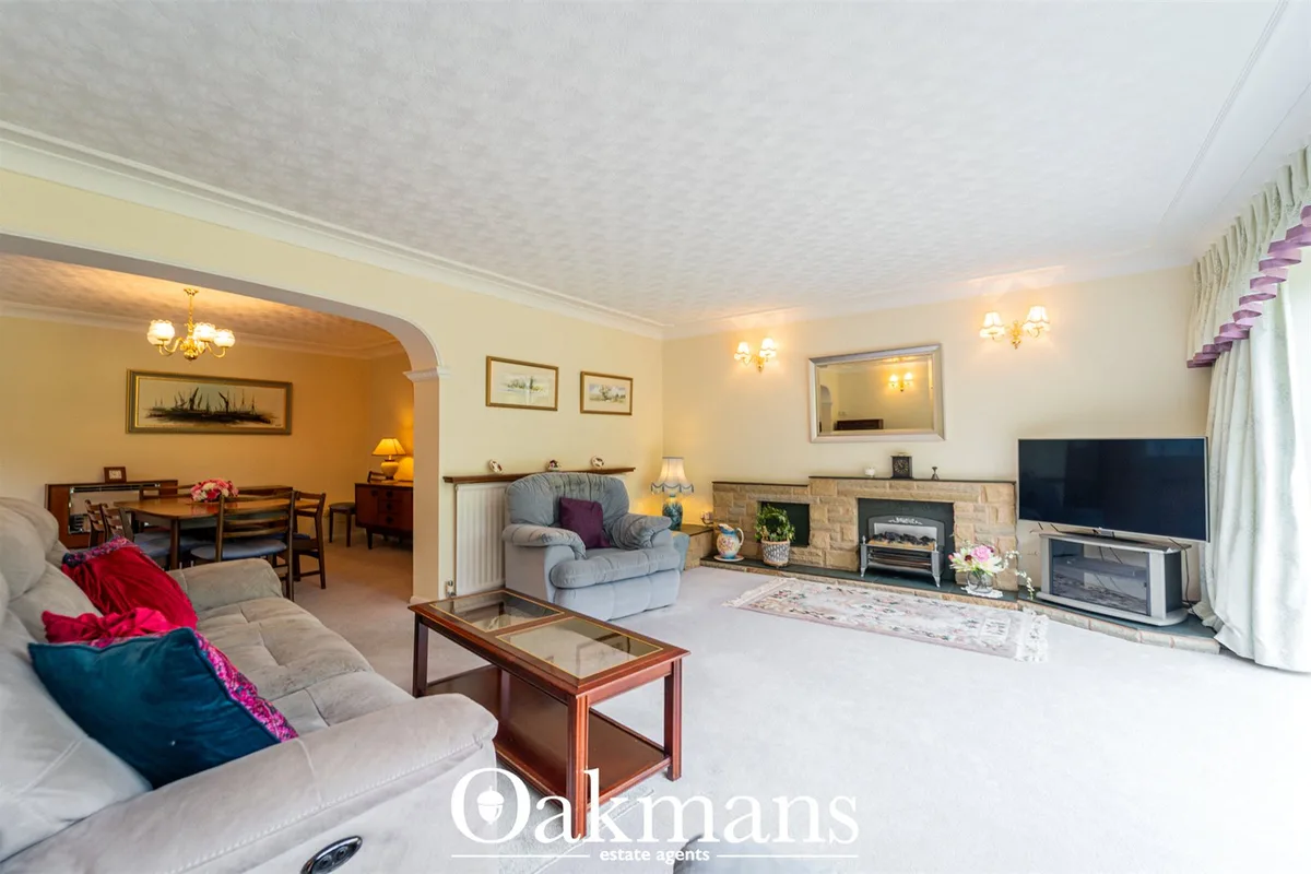 Spacious living room with cream sofa, fireplace, beige armchair, wooden coffee table, TV on stand, framed artwork and do