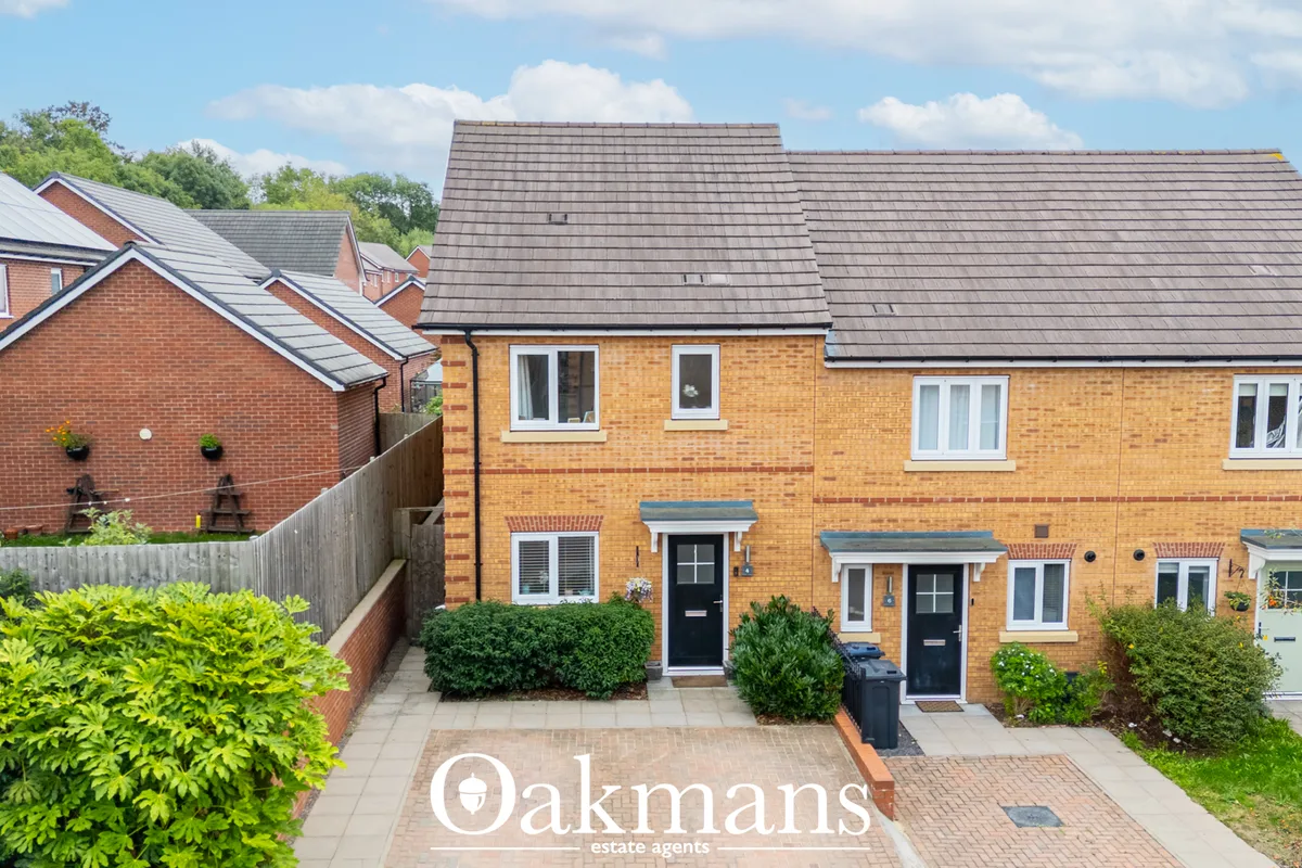Brick townhouses with slate roofs, black doors, paved forecourt and landscaped borders on tree-lined residential street