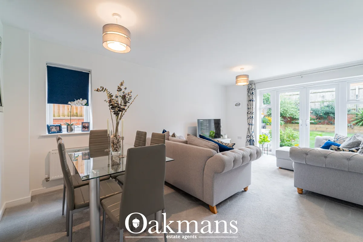 Spacious open-plan living room with beige sofas, dining area with glass table, modern ceiling lights, patio doors to gar