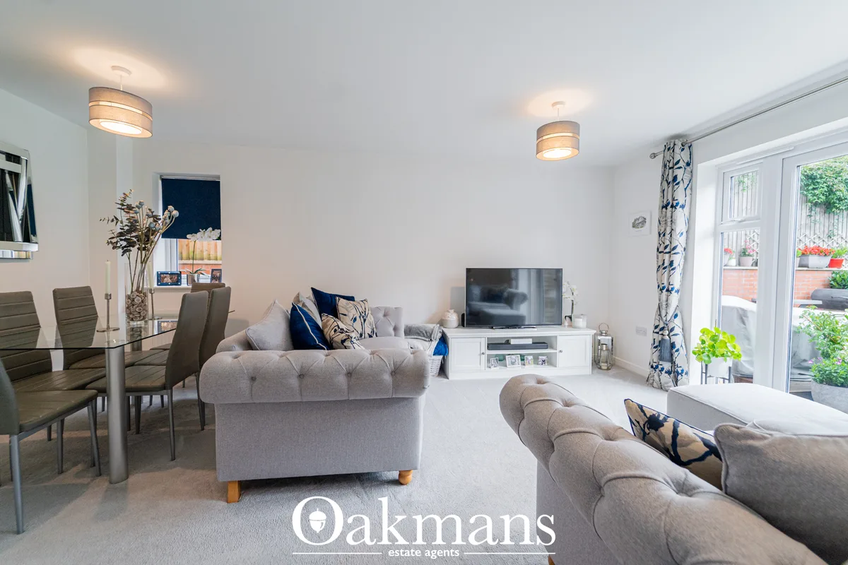 Spacious open-plan living room with grey upholstered furniture, wall-mounted TV, dining area, patio doors to garden and 