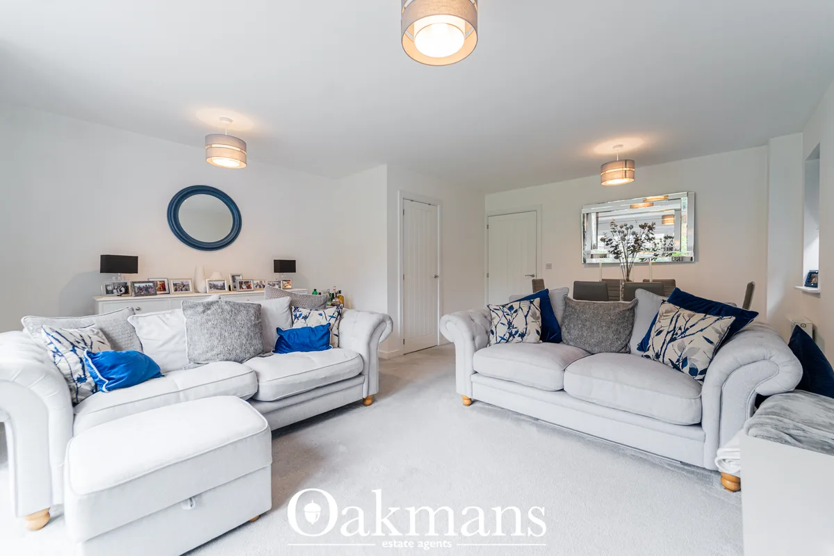 Spacious living room with two cream sofas, blue patterned cushions, grey carpet, ceiling lights, and wall-mounted mirror