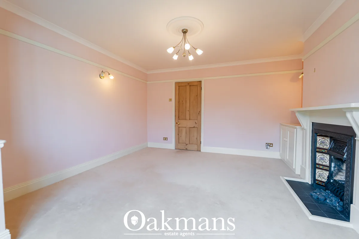 Spacious living room with pink walls, white dado rail, ornamental fireplace with dark insert, wooden door, ceiling light