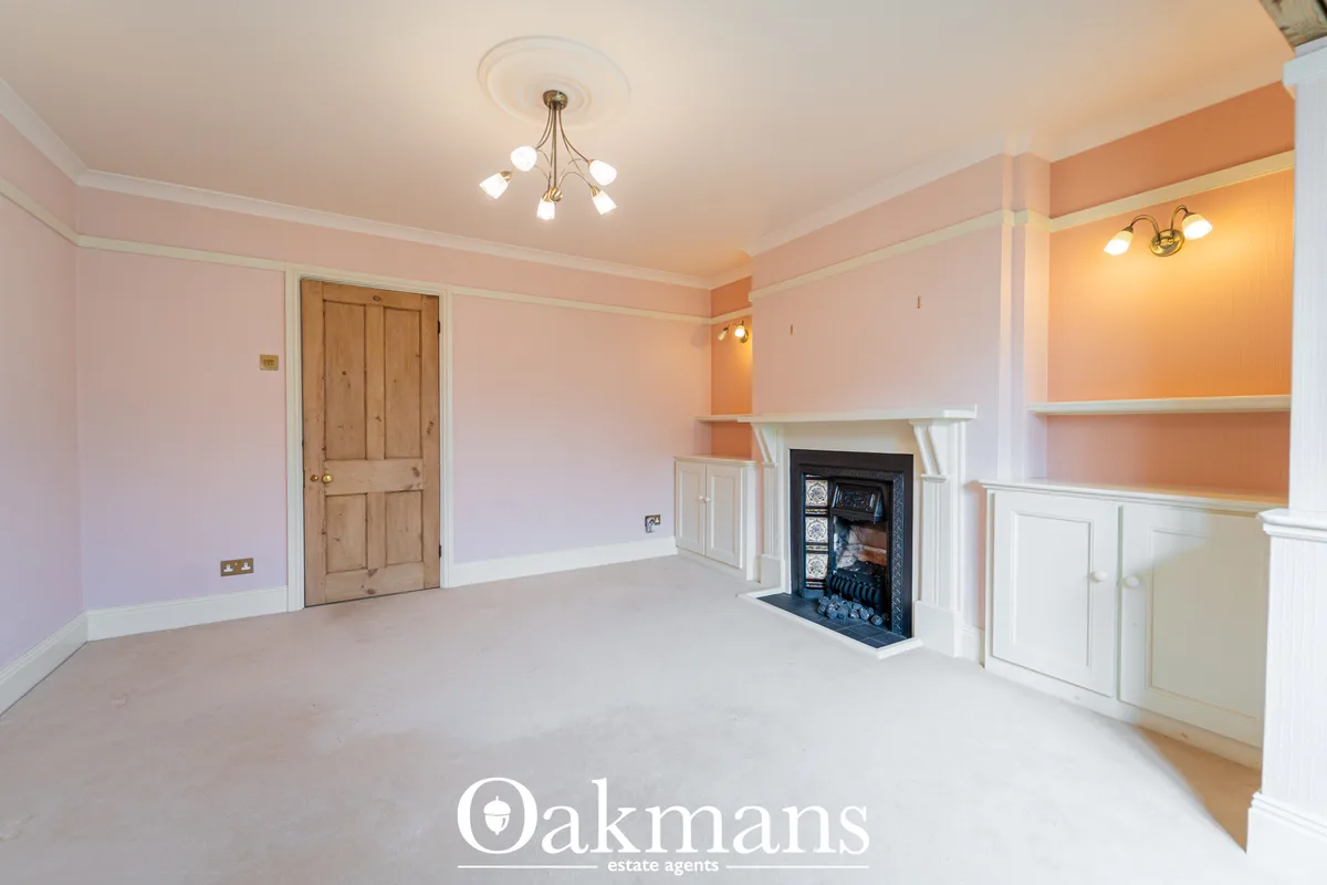 Spacious living room with fireplace, white built-in shelving, wood door, pink walls, ceiling rose and brass light fixtur