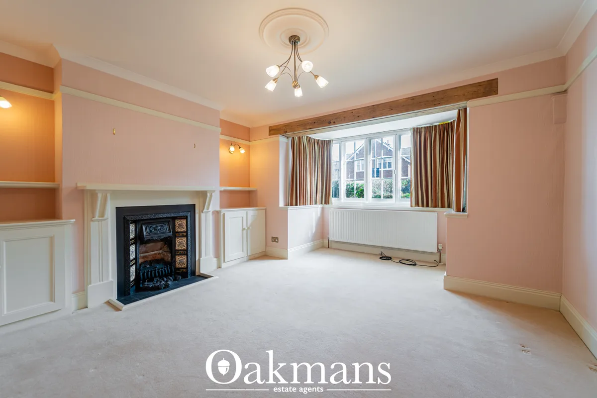 Spacious living room with pink walls, fireplace with black insert, large bay windows with gold curtains, ceiling light f