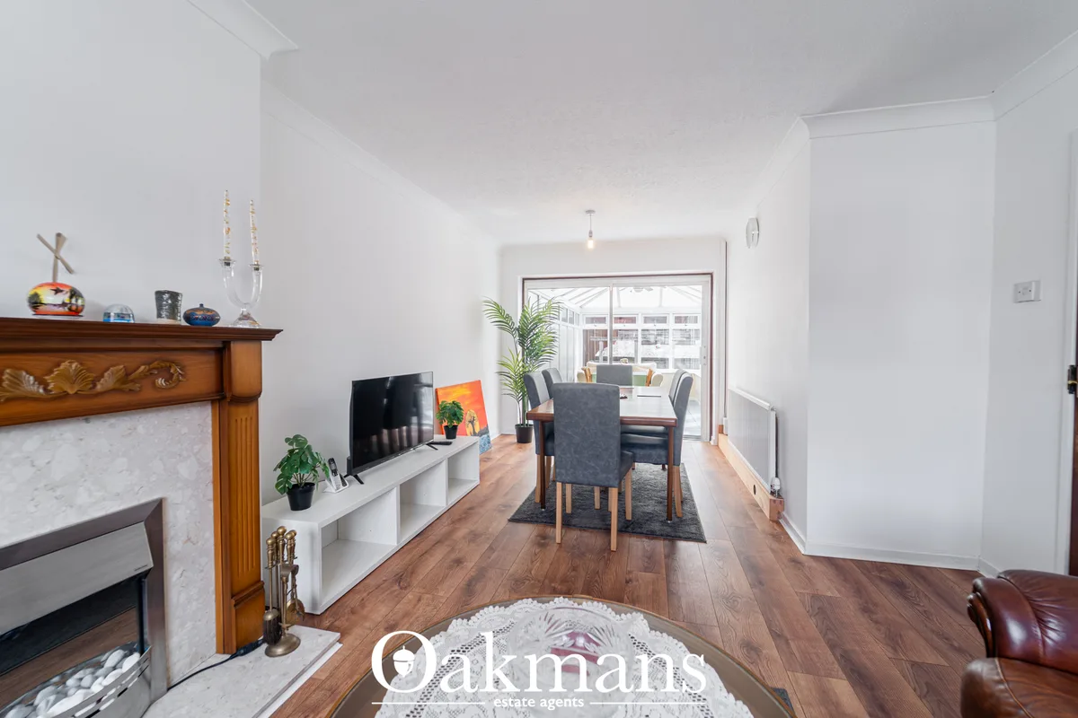 Open-plan living and dining room with wooden fireplace, white TV unit, dining table with grey chairs, wooden flooring, a