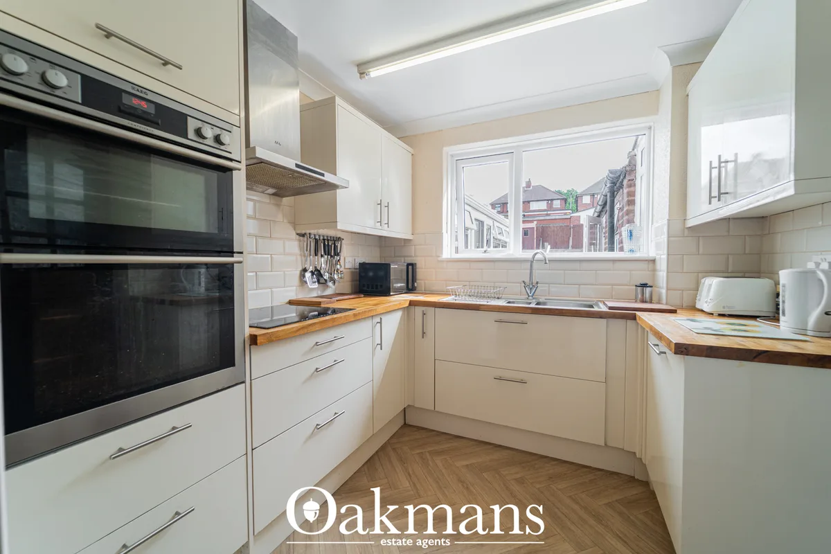 Modern fitted kitchen with cream cabinetry, wooden worktops, stainless steel oven, window overlooking residential street