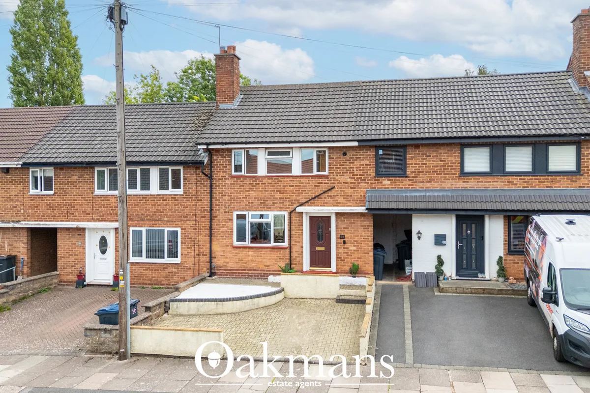 Brick terraced house with driveway, paved forecourt, white entrance door, multiple windows and dark roof tiles