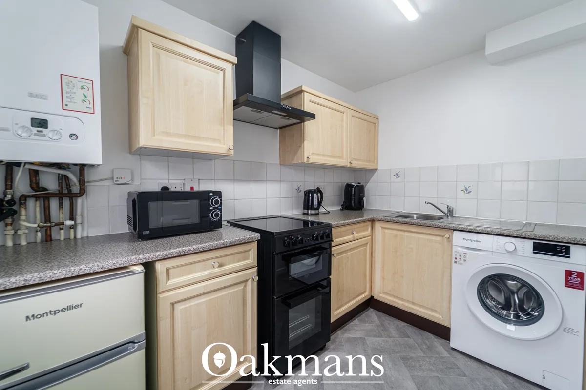 Fitted kitchen with light wood units, black cooker with extractor hood, granite worktops, washing machine and integrated