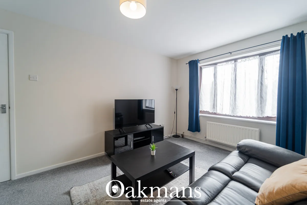 Bright living room with black TV unit, black coffee table, grey sofa, large windows with blue curtains and wooden floori
