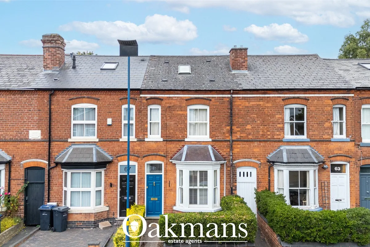 Terrace of red brick Victorian townhouses with slate roofs, white sash windows, blue and black doors, and manicured fron