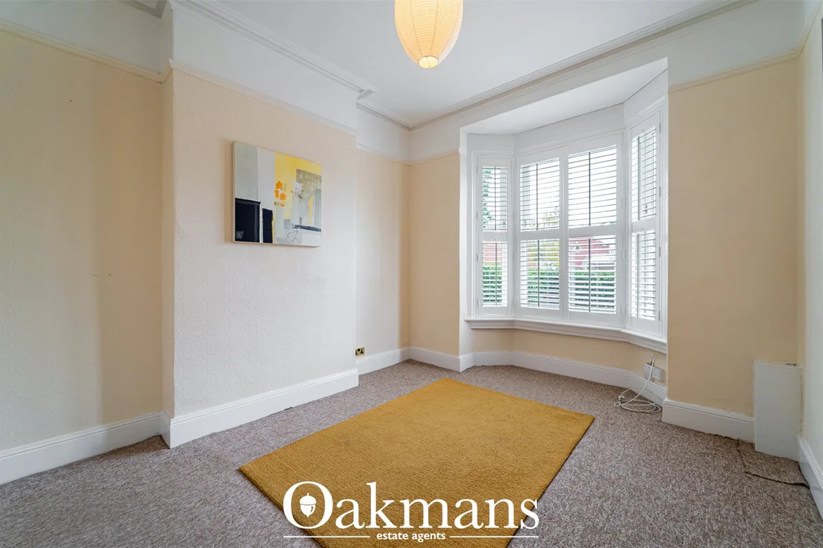 Bright study room with bay window, white shutters, cream walls, carpet flooring, pendant light and small artwork