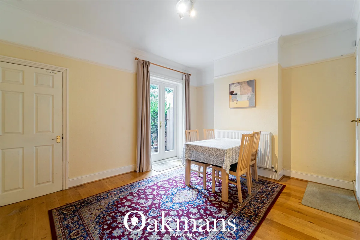 Bright yellow dining room with wooden table, four chairs, patterned rug, French doors to garden, radiator and cream fitt