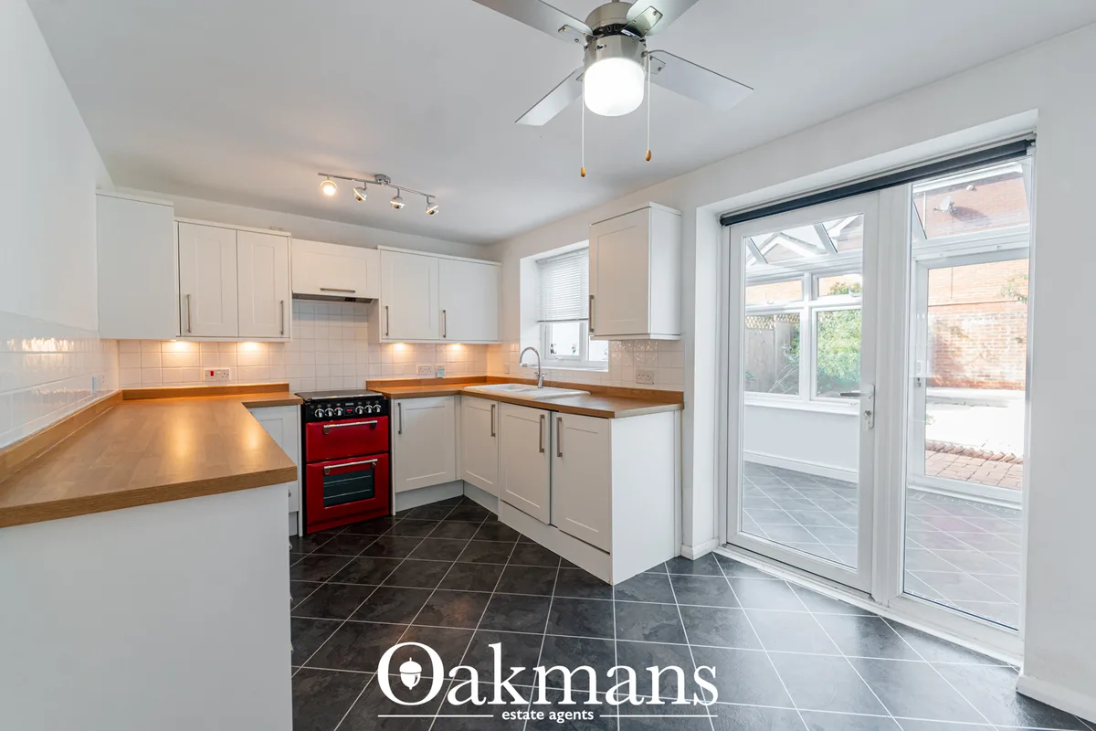 Modern fitted kitchen with white units, wooden worktops, red range cooker, dark tile flooring and patio doors to garden