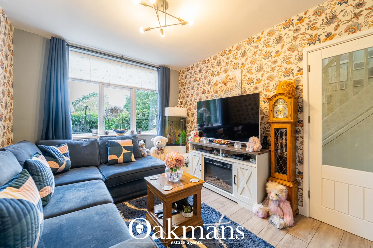 Living room with blue sofa, floral wallpaper, flat-screen TV on white media unit, wooden coffee table, large windows wit