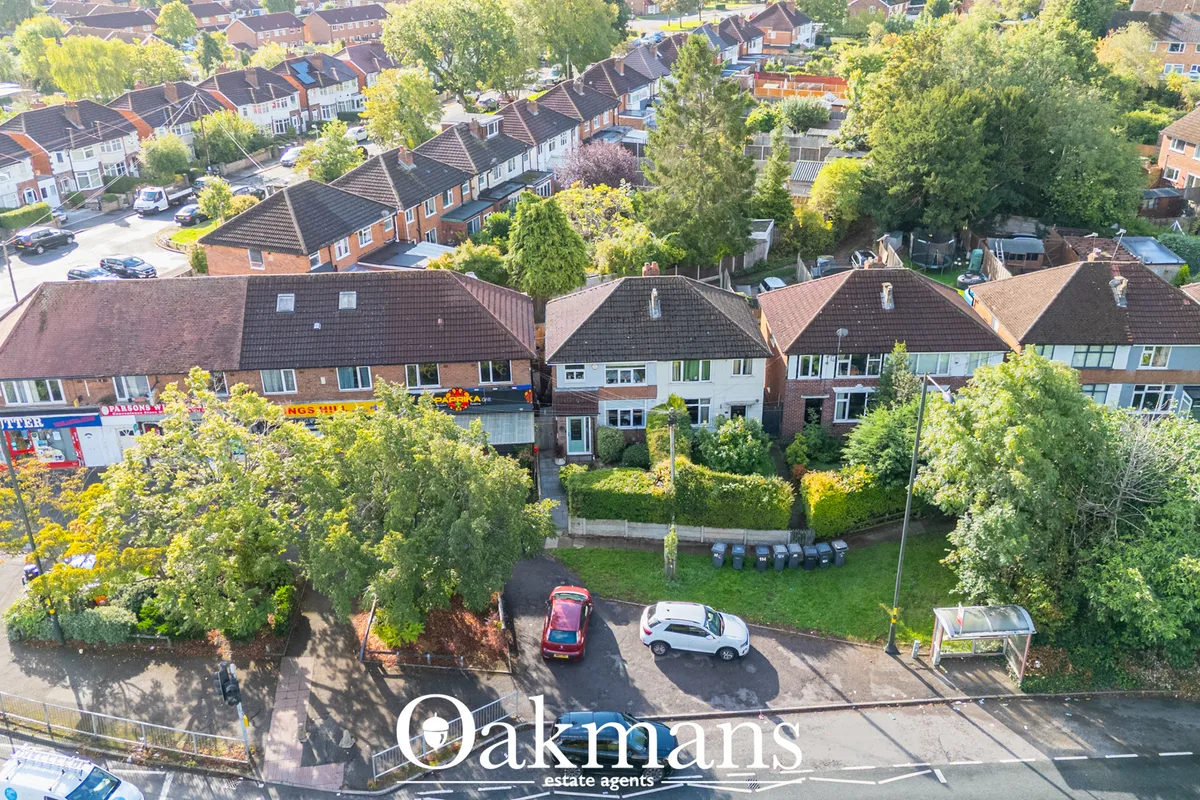 Aerial drone photograph of suburban residential street with semi-detached brick houses, driveways, parked cars, mature t