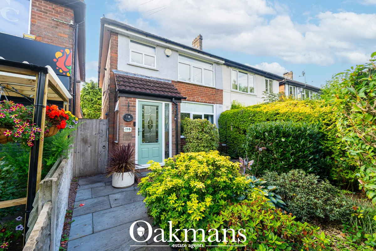 Brick and render semi-detached house with light turquoise door, well-maintained front garden with shrubs and flowering p