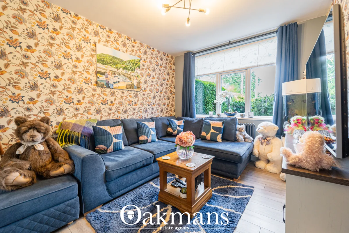 Blue upholstered L-shaped sofa with patterned cushions, wooden coffee table, large bay windows with blue curtains, flora