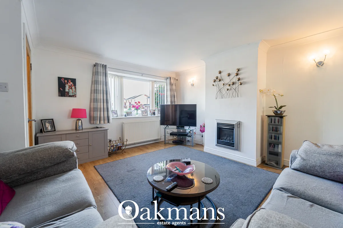 Bright living room with grey sofas, fireplace, flat-screen TV, wooden flooring, blue rug and large window with garden vi