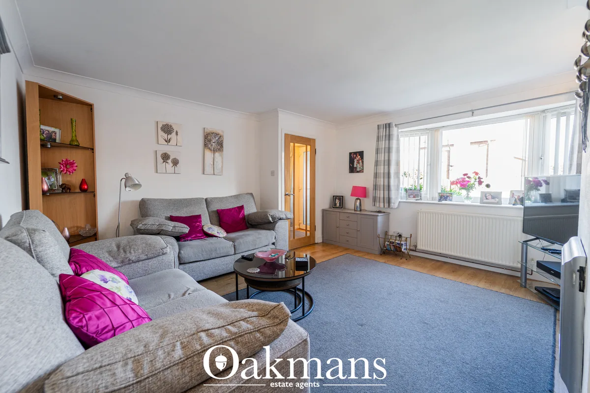 Spacious living room with grey corner sofa, magenta scatter cushions, blue carpet, wooden shelving, and large bay window