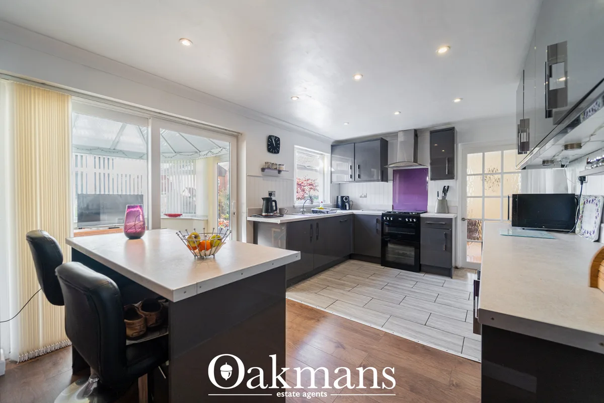Modern open-plan kitchen with dark cabinetry, white worktops, purple splashback, black range cooker, and island breakfas