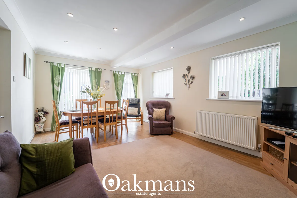 Spacious open-plan living room with cream walls, wooden flooring, dining table with chairs, burgundy armchair, TV on woo