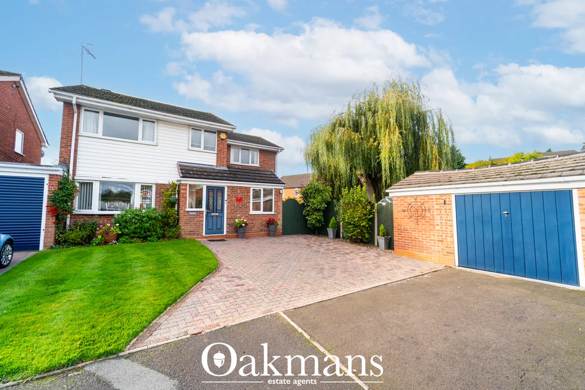 Red brick and white detached house with brick paved driveway, manicured lawn, blue garage doors, and mature weeping will