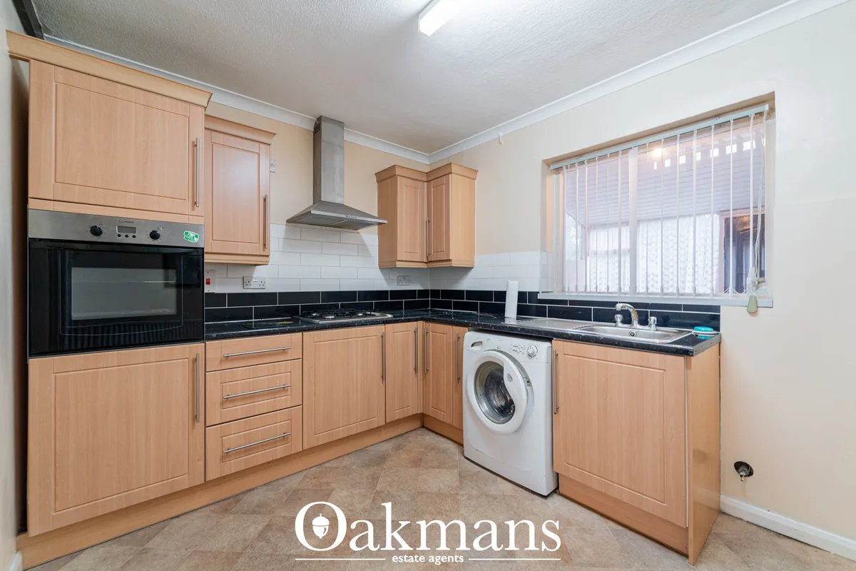 Modern fitted kitchen with wooden units, black granite worktops, built-in oven, hob with extractor hood, washing machine