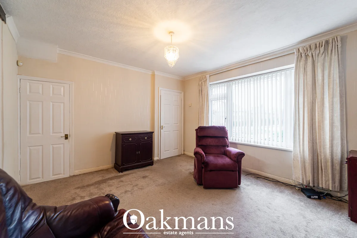 Spacious living room with beige walls, burgundy armchair, dark wood cabinet, large window with vertical blinds and cream