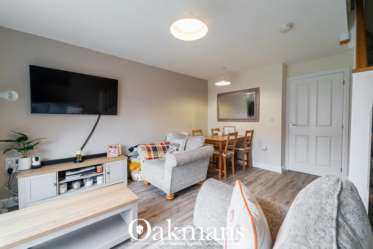 Open-plan living room with grey upholstered armchairs, wooden dining table with chairs, wall-mounted TV, recessed ceilin