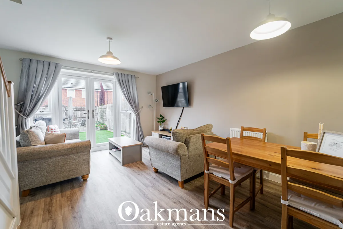 Open-plan living and dining area with grey upholstered armchairs, wooden dining table, wall-mounted TV, patio doors to g