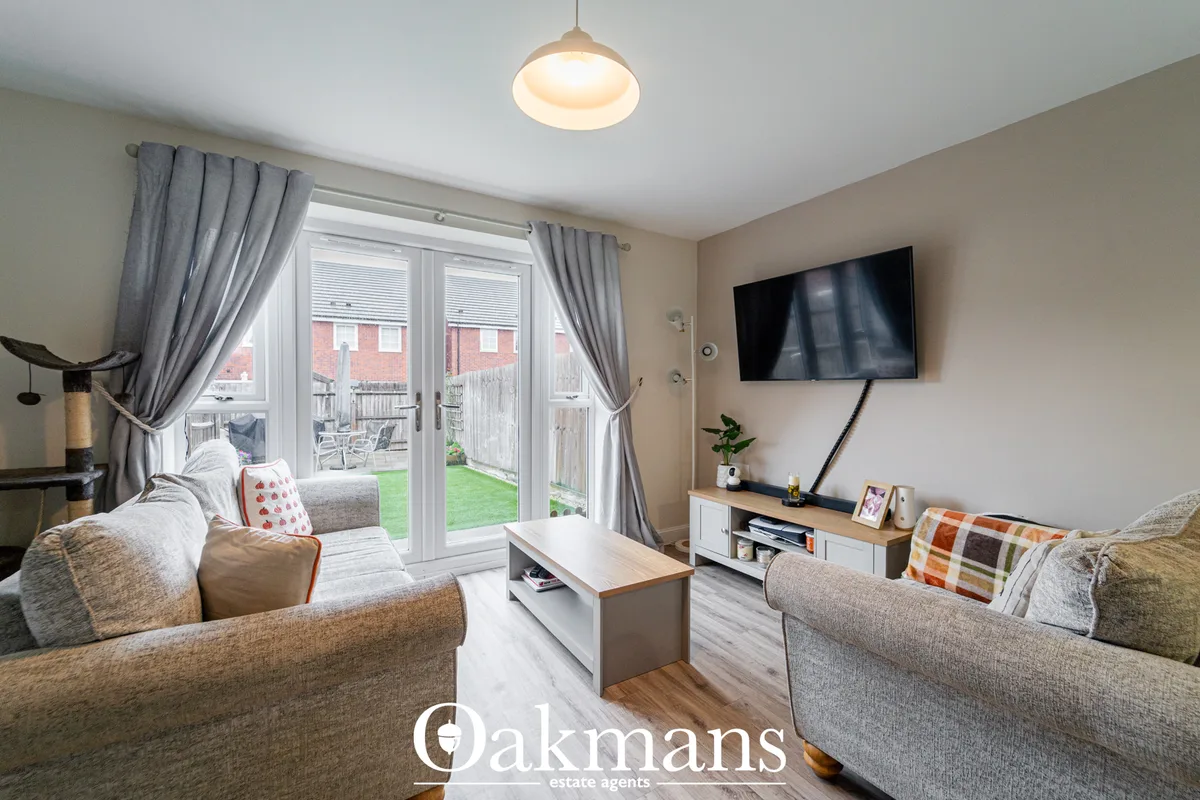 Bright living room with two grey sofas, wall-mounted TV, wooden flooring, grey curtains, pendant light, and patio doors 