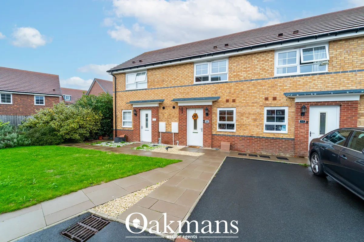 Modern brick townhouse with driveway, lawn and parked car, under blue sky with clouds