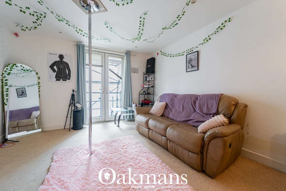 Spacious living room with tan leather sofa, pink rug, pole for fitness, glass doors to balcony, large mirror, and decora