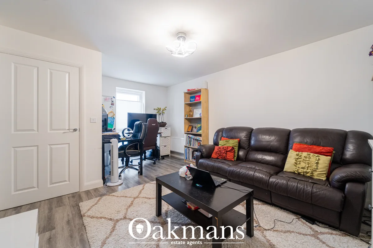 Spacious living room with dark leather reclining sofa, black coffee table, patterned rug, wooden shelving unit, desk are