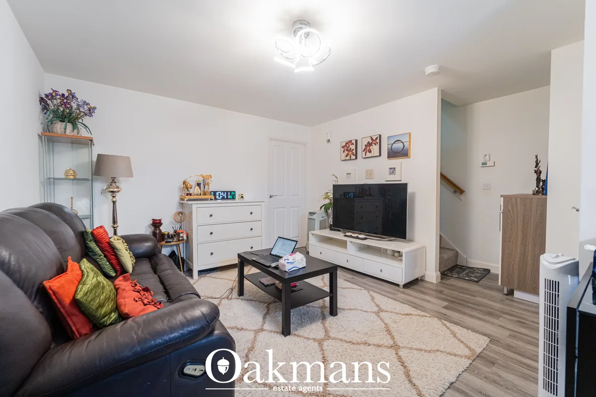 Spacious living room with dark leather sofa, colorful cushions, black coffee table, flat-screen TV on white media unit, 
