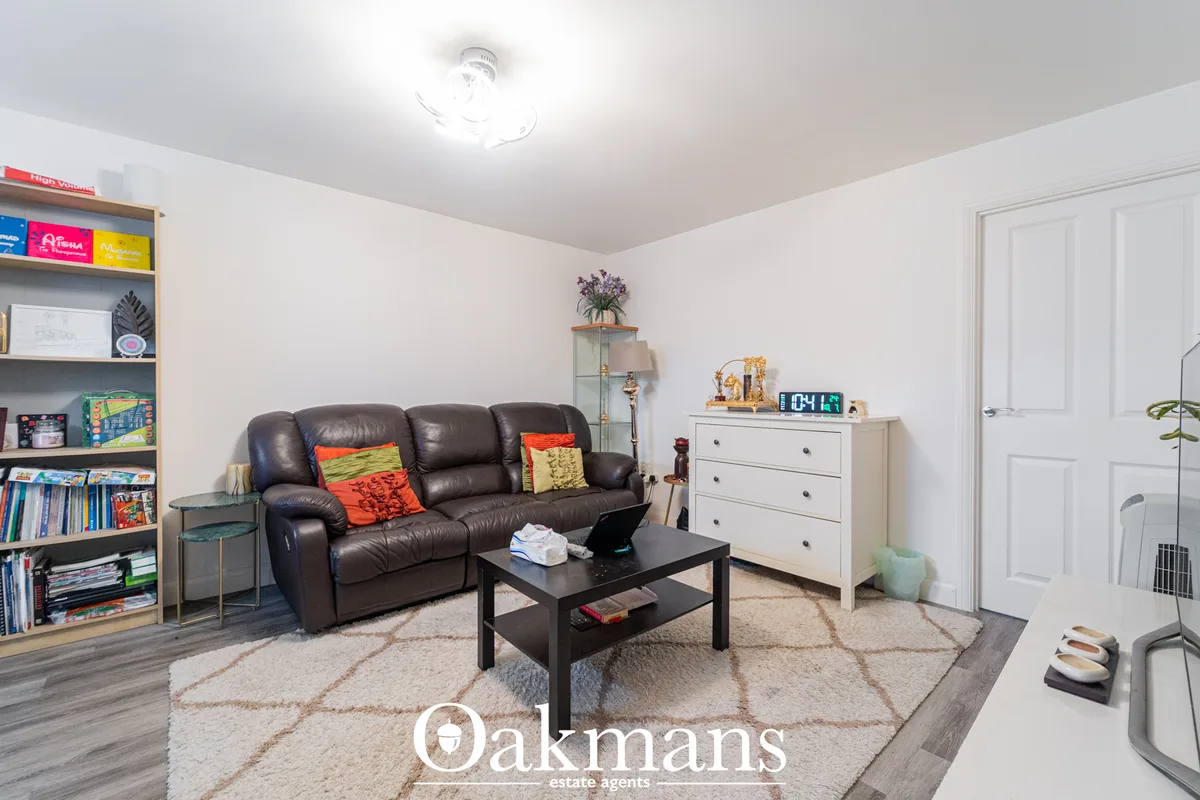 Spacious living room with dark leather sofa, black coffee table, white dresser, geometric area rug, built-in shelving wi