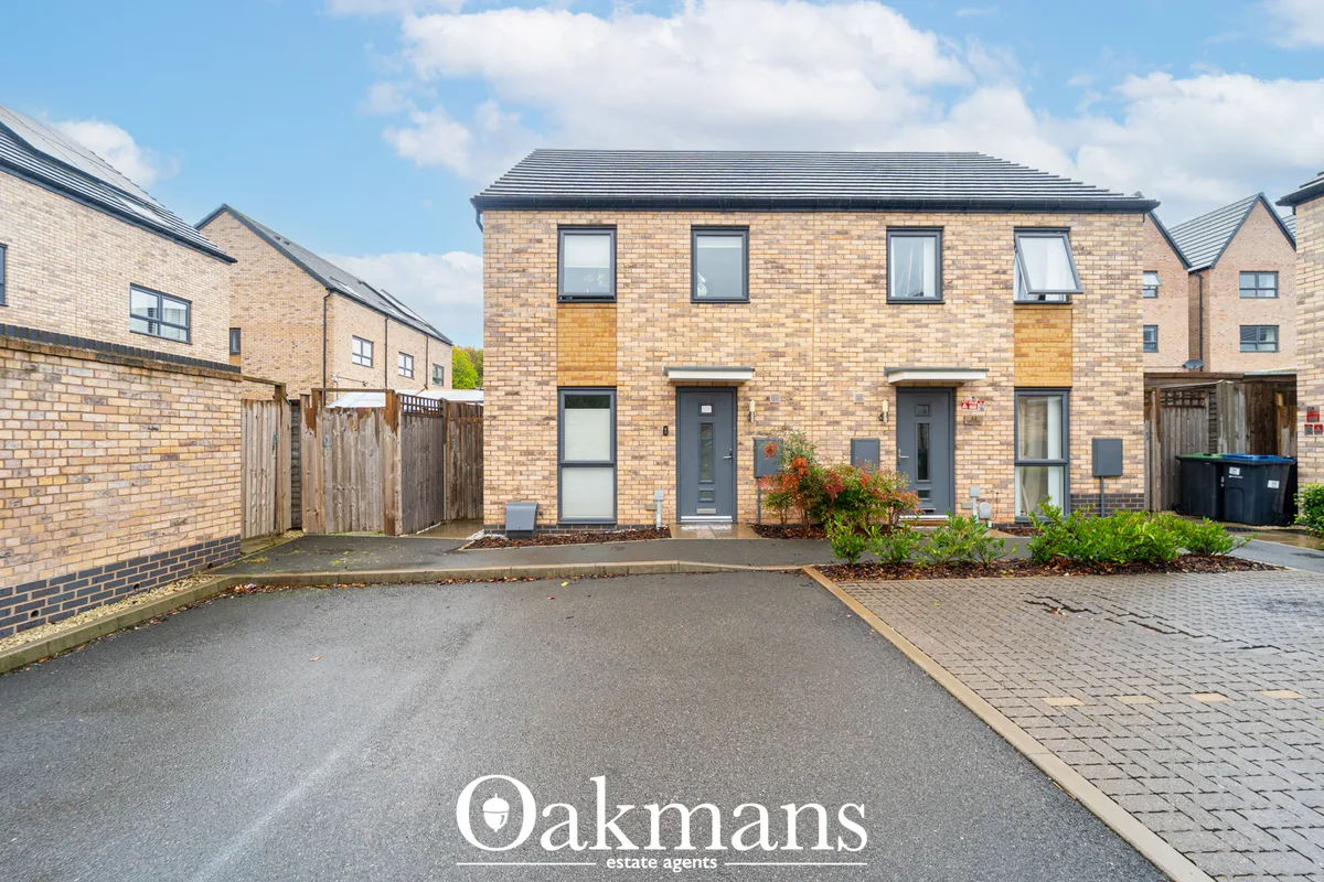 Modern brick-built semi-detached house with slate roof, grey doors, four upper windows, driveway and landscaped front ga
