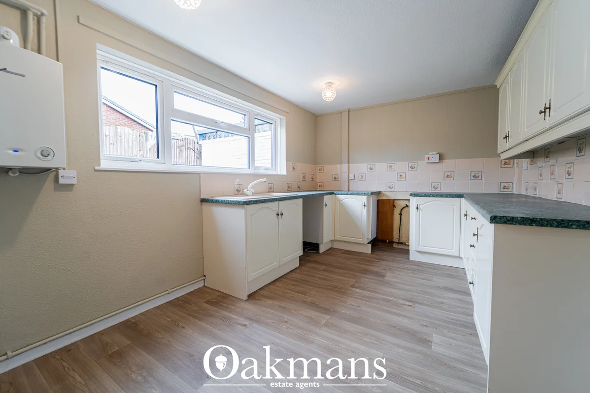 Spacious kitchen with white fitted units, green granite worktops, wooden flooring, large window, and tiled splashback wi