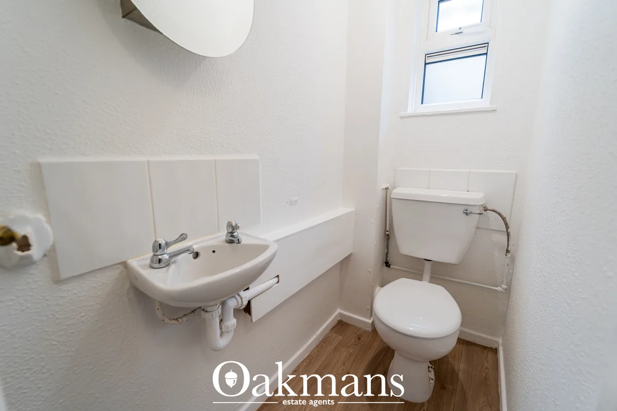 Clean white bathroom with wall-mounted sink, toilet, tiled splashback, small window and wooden flooring