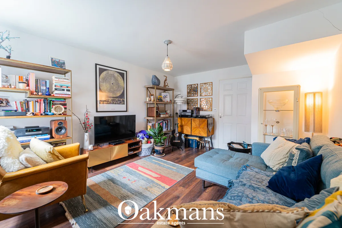 Open-plan living room with blue sofa, tan armchair, wood shelving, TV unit, pendant lighting and wooden flooring through