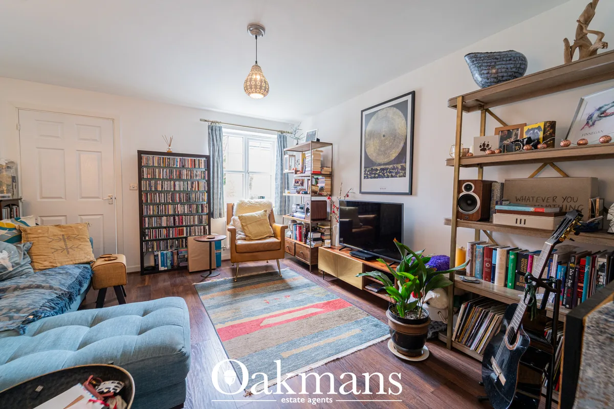 Bright living room with blue sofa, tan leather armchair, wooden shelving, TV unit, large window with blue curtains, hard