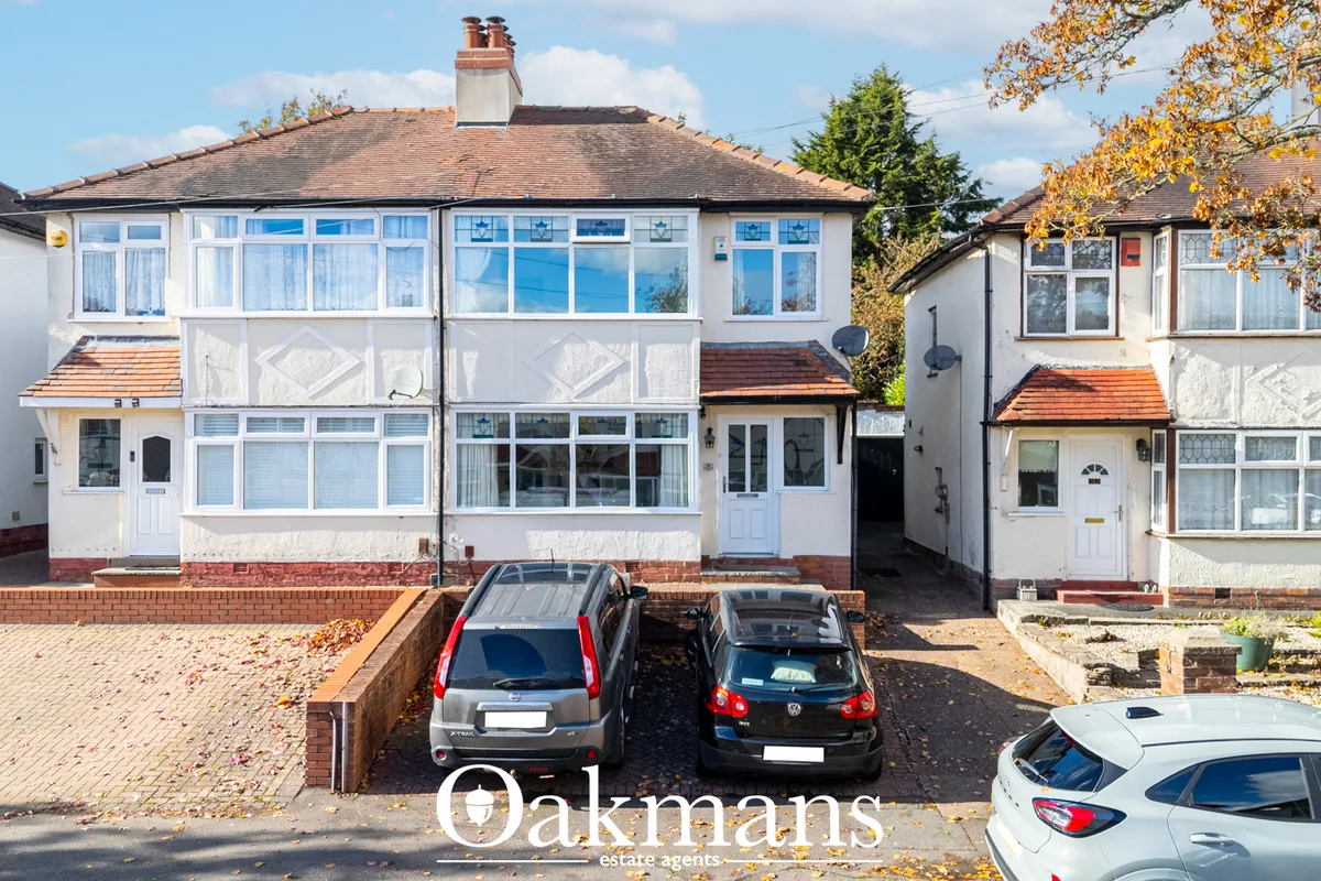 Semi-detached suburban home with white render, red brick base, tile roof and large bay windows. Three cars parked on dri