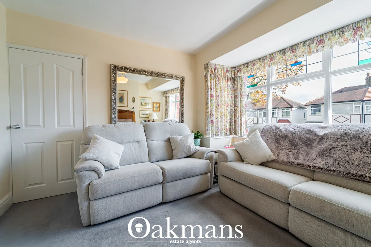 Bright living room with light grey upholstered sofas, cream cushions, floral curtains, large bay windows overlooking res