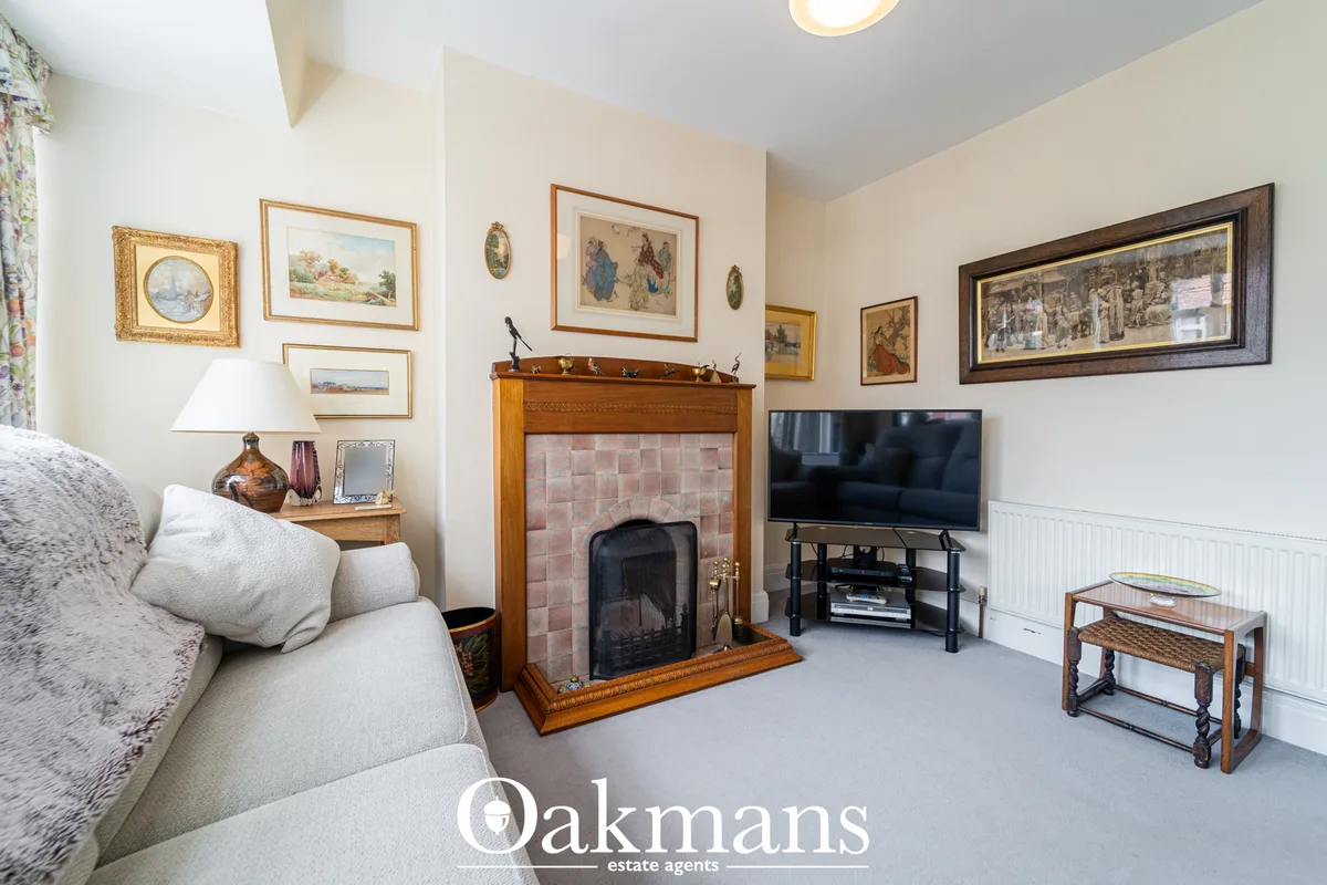 Elegant living room with cream walls, fireplace with pink tile surround, flat-screen TV, grey carpet, upholstered sofa, 