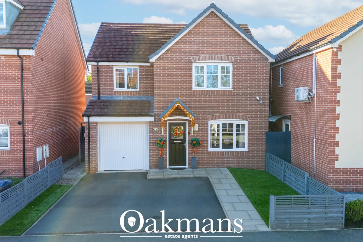 Red brick detached house with white garage door, dark green entrance door decorated with wreath, driveway and manicured 