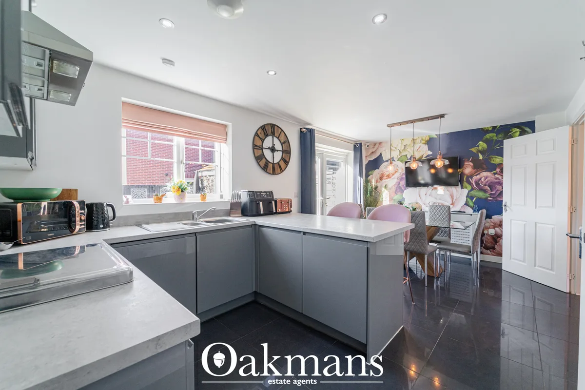 Modern open-plan kitchen with dark grey cabinetry, white worktops, sink with window, dining area, floral wallpaper and p