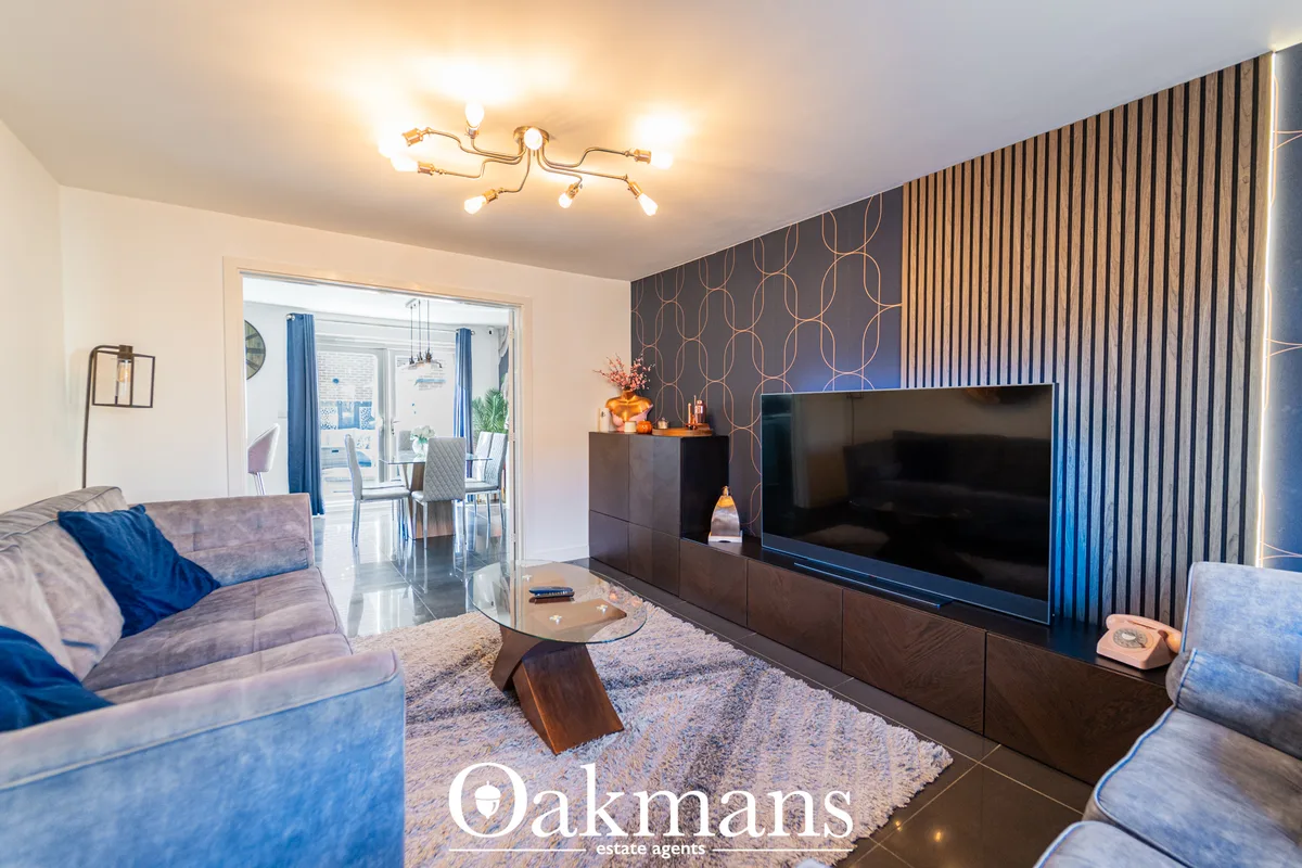 Contemporary living room with grey sectional sofas, wall-mounted flat-screen TV on dark media unit, geometric wallpaper,