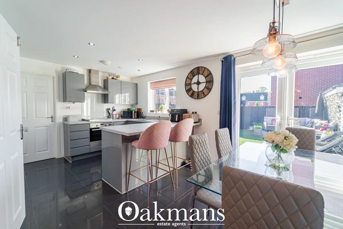 Modern open-plan kitchen with grey fitted units, white worktops, breakfast bar with pink and beige quilted bar stools, p