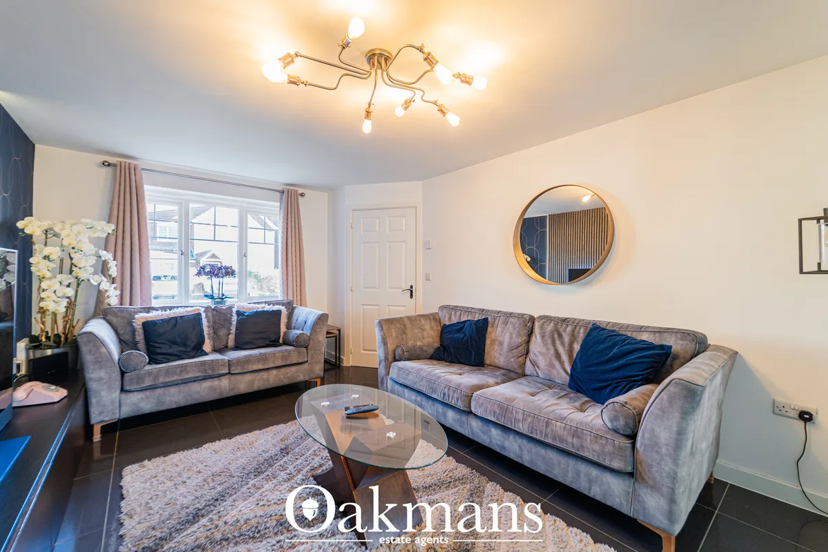 Spacious living room with two grey sofas, blue velvet cushions, glass coffee table, circular gold-framed mirror, and lar