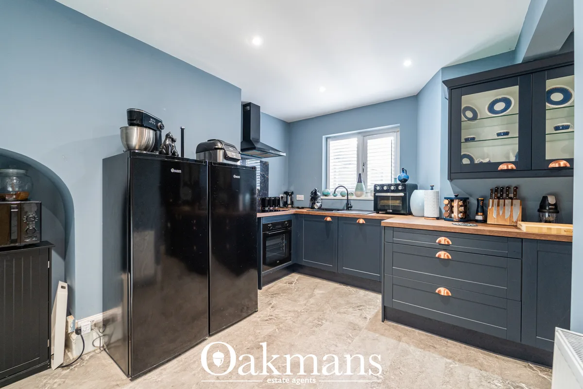 Modern fitted kitchen with charcoal grey cabinetry, wooden worktops, black appliances, and blue-painted walls with reces